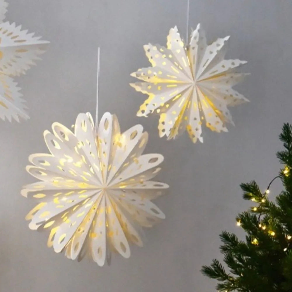 Valaistut valkoiset paperilumihiutaleet joulukuusen vieressä